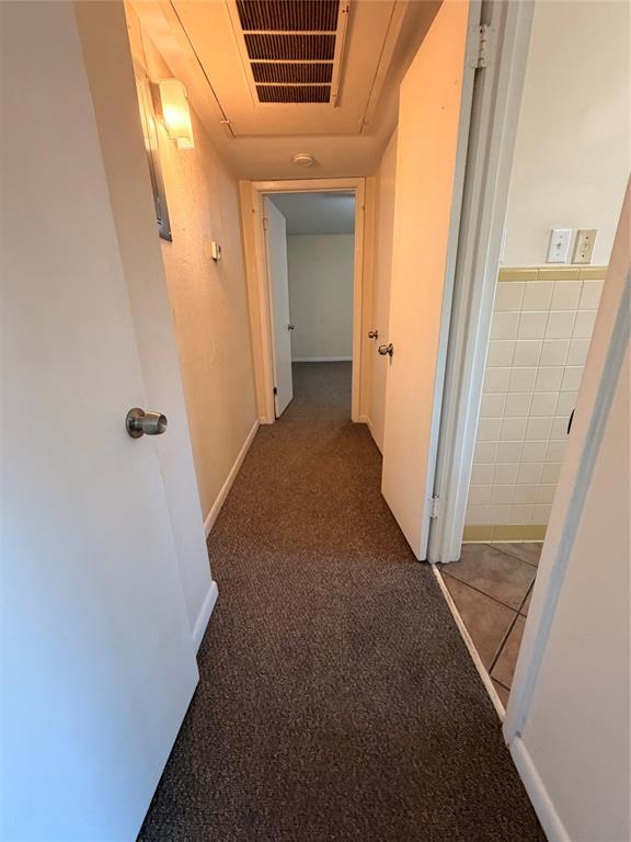 Hallway featuring neutral carpeting, wall-mounted light fixtures, and solid-core interior doors with metallic hardware