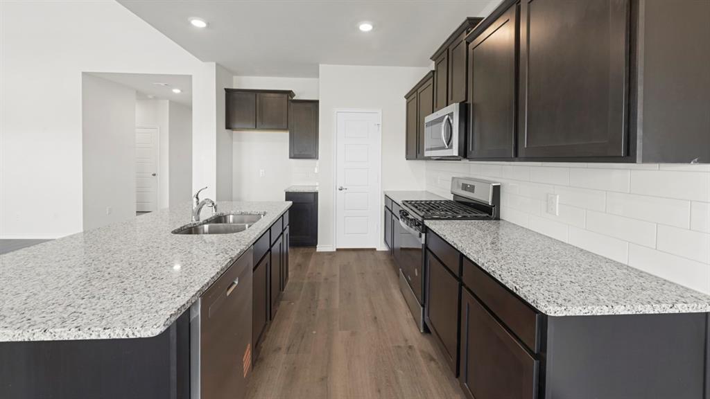 Galley-style kitchen featuring dark cabinetry, speckled quartz countertops, stainless steel appliances including a gas cooktop and built-in microwave, subway tile backsplash, and wood-finish flooring throughout Galley-style kitchen featuring dark cabinetry, speckled quartz countertops, stainless steel appliances including a gas cooktop and built-in microwave, subway tile backsplash, and wood-finish flooring throughout