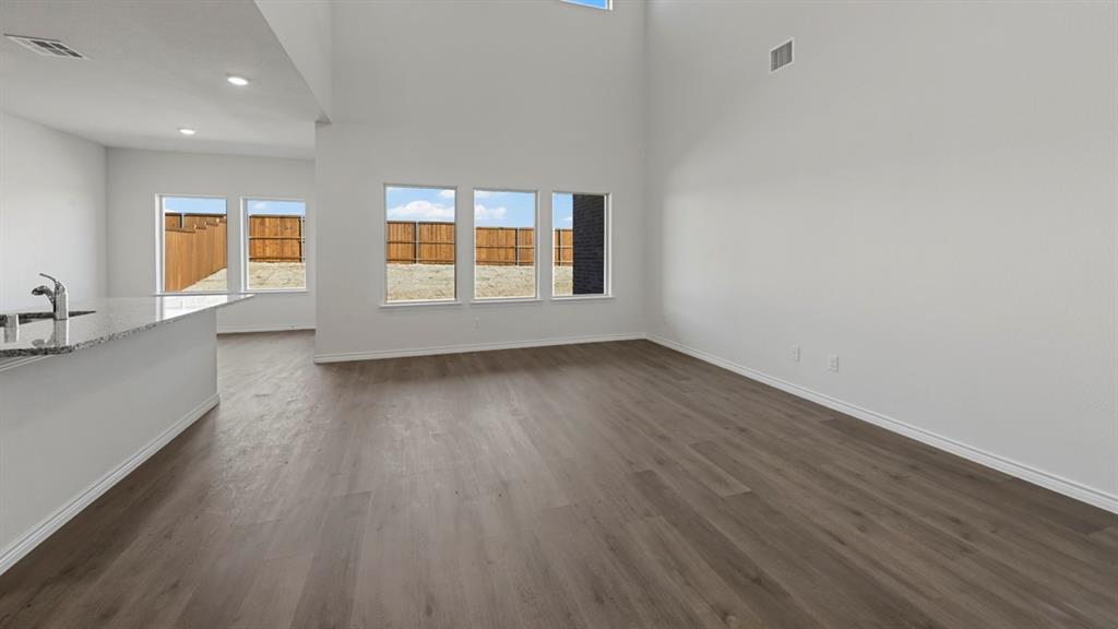 Open concept living area featuring high ceilings, recessed lighting, wood-finish flooring, a kitchen island with a stone countertop, and multiple windows with outdoor views