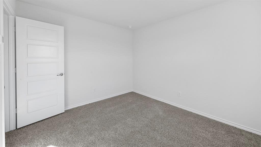 Spacious bedroom featuring neutral wall finishes, a clean white six-panel entry door, and soft gray carpet flooring throughout