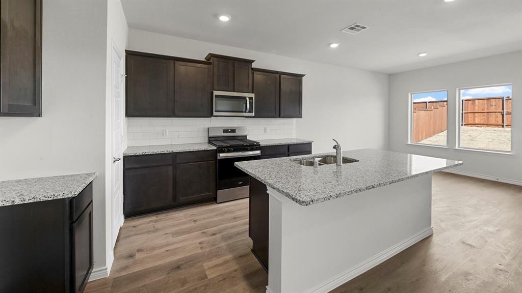 Modern kitchen featuring dark cabinetry, stainless steel appliances, and a spacious island with quartz countertop Modern kitchen featuring dark cabinetry, stainless steel appliances, and a spacious island with quartz countertop