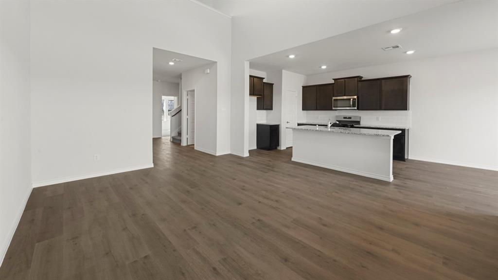 Open-concept living space featuring wood-finish flooring, a kitchen island with stone countertop, dark cabinetry, stainless steel appliances, and recessed lighting