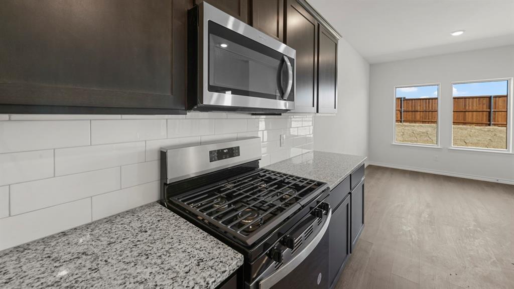 Kitchen featuring stainless steel appliances, granite-style countertops, dark wood-finish cabinetry, and a subway tile backsplash Kitchen featuring stainless steel appliances, granite-style countertops, dark wood-finish cabinetry, and a subway tile backsplash