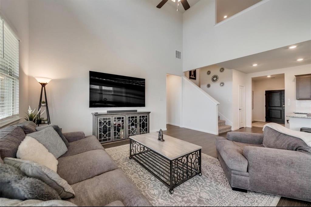 Living area featuring a soaring ceiling, wood-finish flooring, a contemporary staircase, an upper-level overlook, and recessed lighting
