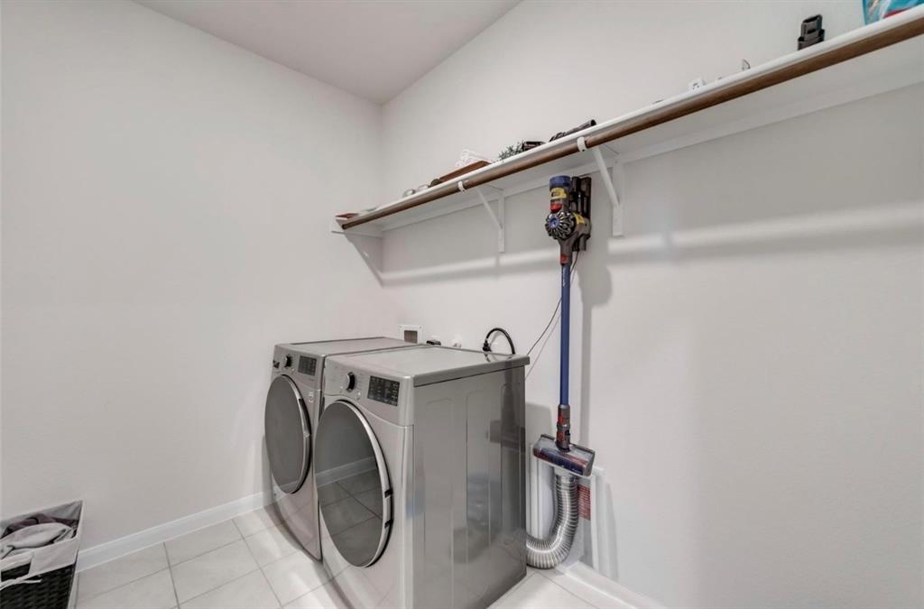 Modern laundry room featuring stacked front-load washer and dryer with chrome hardware, white subway tile flooring, and wall-mounted drying rod with integrated storage system