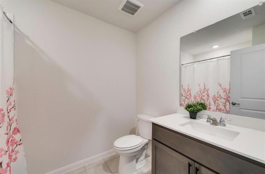 Bathroom featuring a gray vanity with a white countertop and integrated sink, a large wall-mounted mirror, and tile flooring