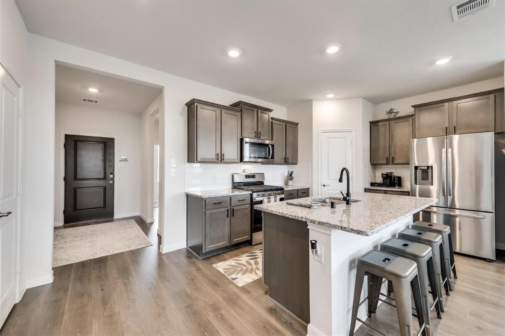 Kitchen with wood-finish flooring, recessed lighting, white subway tile backsplash, stainless steel appliances, and a central island featuring a stone countertop and seating area
