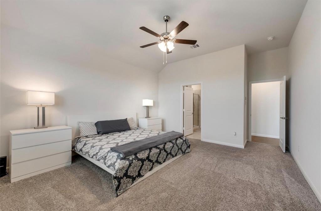 Spacious primary bedroom featuring neutral carpeting, abundant natural light from multiple windows, and a ceiling fan with integrated lighting