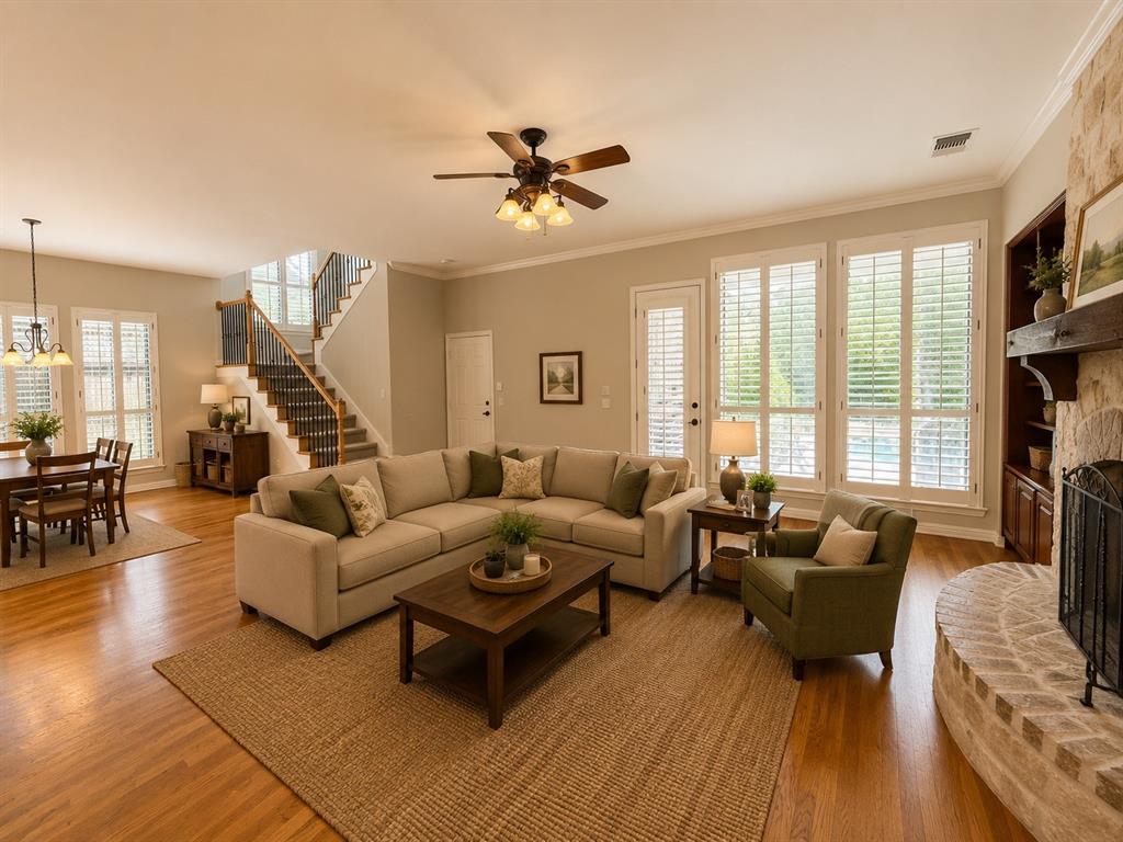 Spacious living area featuring wood-finish flooring, a stone fireplace with a substantial wood mantle, and a ceiling fan with integrated lighting