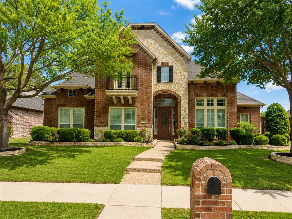Brick and stone facade residence featuring a prominent arched entry, second-story balcony with iron railing, and decorative window shutters