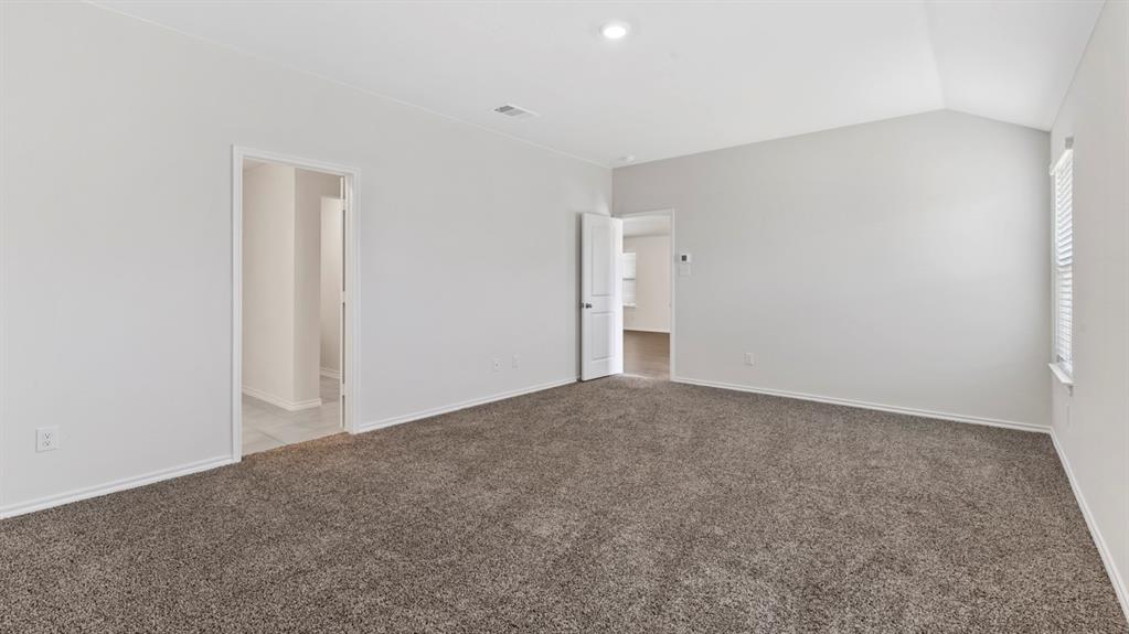 Spacious room featuring vaulted ceilings, neutral-toned walls, and plush grey carpeting