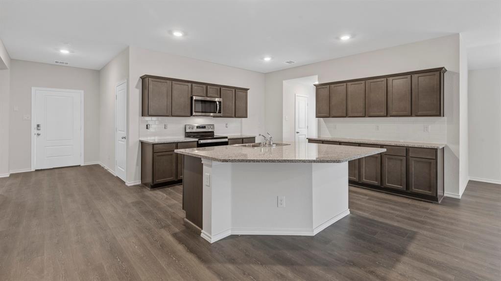 Spacious kitchen featuring a large island with sink, ample cabinetry, granite-finish countertops, stainless steel appliances, and wood-finish flooring
