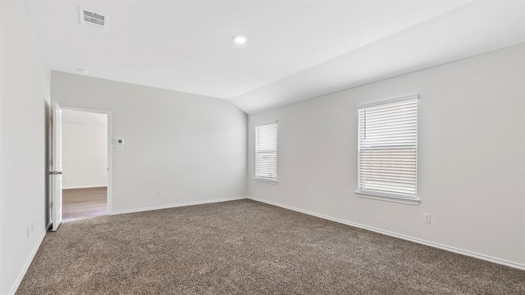 Spacious room featuring vaulted ceilings, neutral-toned carpeting, and two windows with blinds