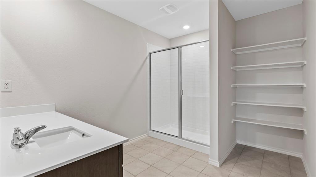 Bathroom featuring a single vanity with an integrated sink, a glass-enclosed shower, and built-in shelving