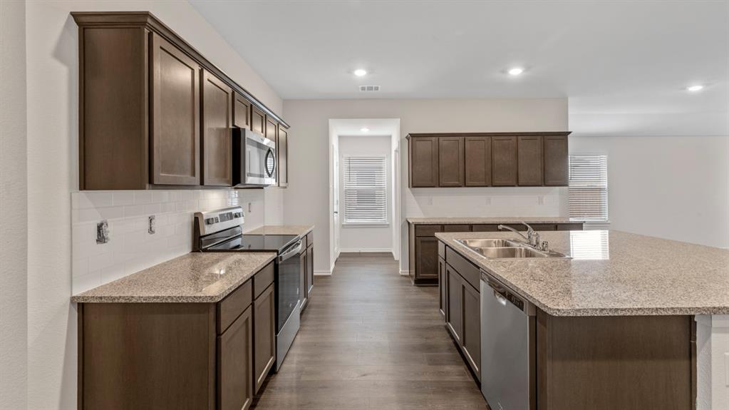 Open-concept kitchen featuring dark wood cabinetry, granite countertops, and stainless steel appliances, including a range, microwave, and dishwasher