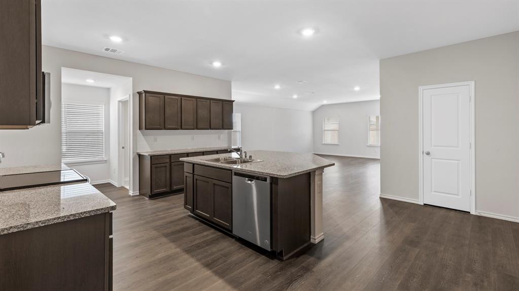 Spacious kitchen featuring dark wood cabinetry, granite countertops, a central island with a stainless steel dishwasher, and recessed lighting