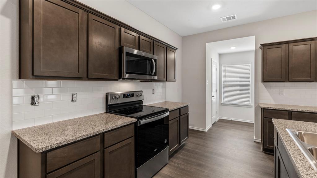 Kitchen featuring dark wood-finish cabinetry, stainless steel appliances, granite-style countertops, white subway tile backsplash, and wood-finish flooring