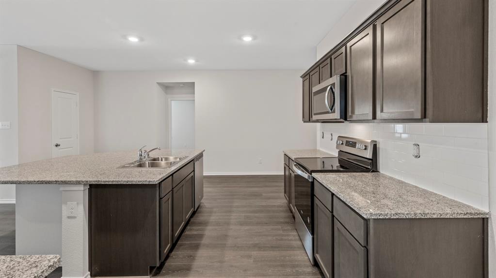 Kitchen featuring dark wood-finish cabinetry, light speckled countertops, stainless steel appliances, and a subway tile backsplash