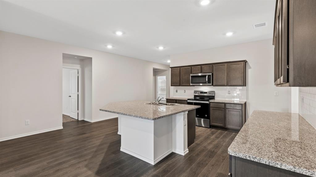 Open-concept kitchen featuring dark wood cabinetry, stainless steel appliances, granite countertops, and a white subway tile backsplash