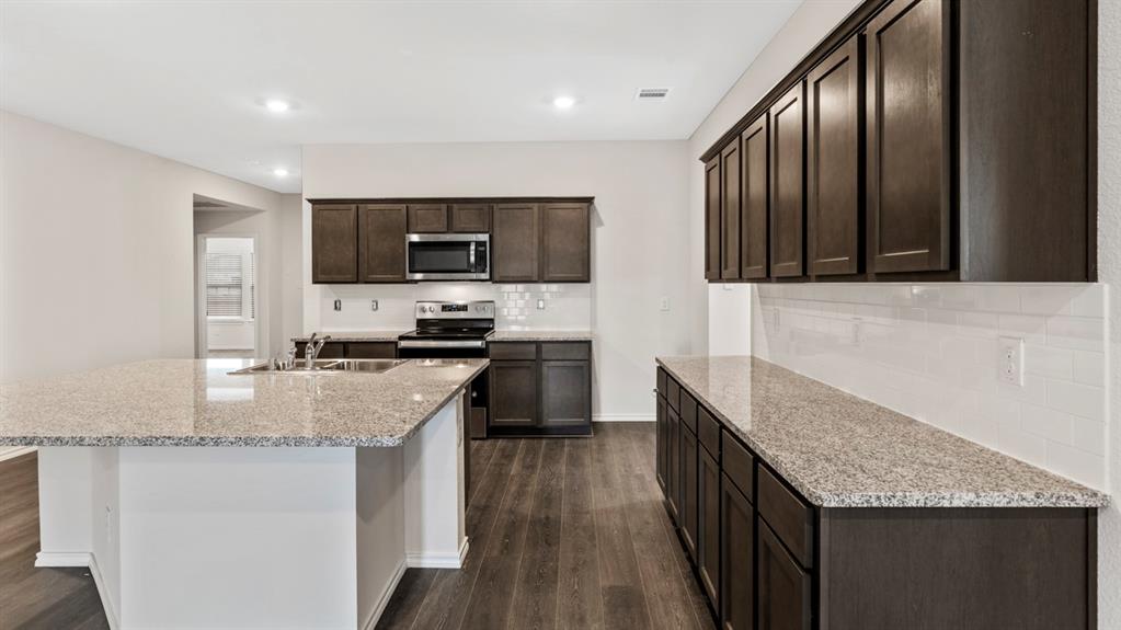 Kitchen featuring dark wood-finish cabinetry, light speckled countertops, a subway tile backsplash, and wood-finish flooring