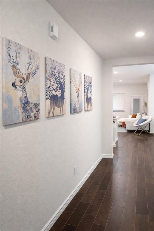 Hallway featuring rich wood-finish flooring, white baseboards, and recessed lighting