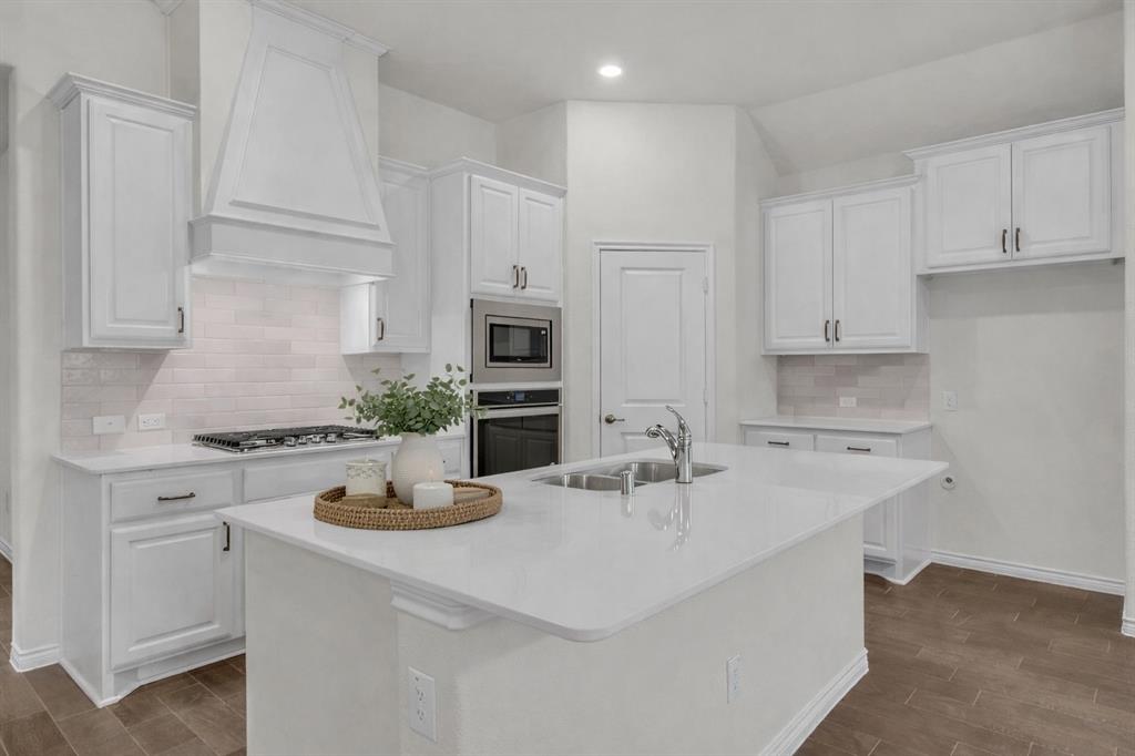 Modern kitchen featuring a large central island with an undermount sink, white cabinetry, integrated stainless steel appliances, a tile backsplash, and wood-finish flooring