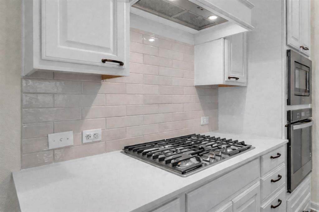 Kitchen with stainless steel gas cooktop, light-toned subway tile backsplash, white shaker cabinetry, and light-toned countertops