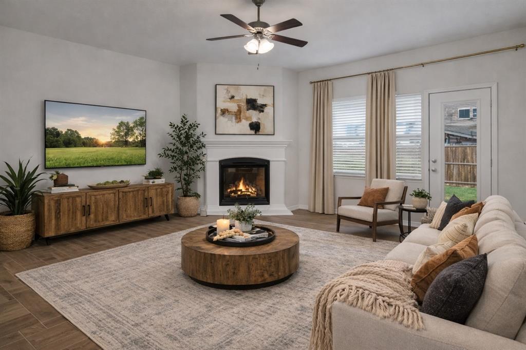 Living area featuring wood-finish flooring, a corner fireplace with a white mantel, and a ceiling fan