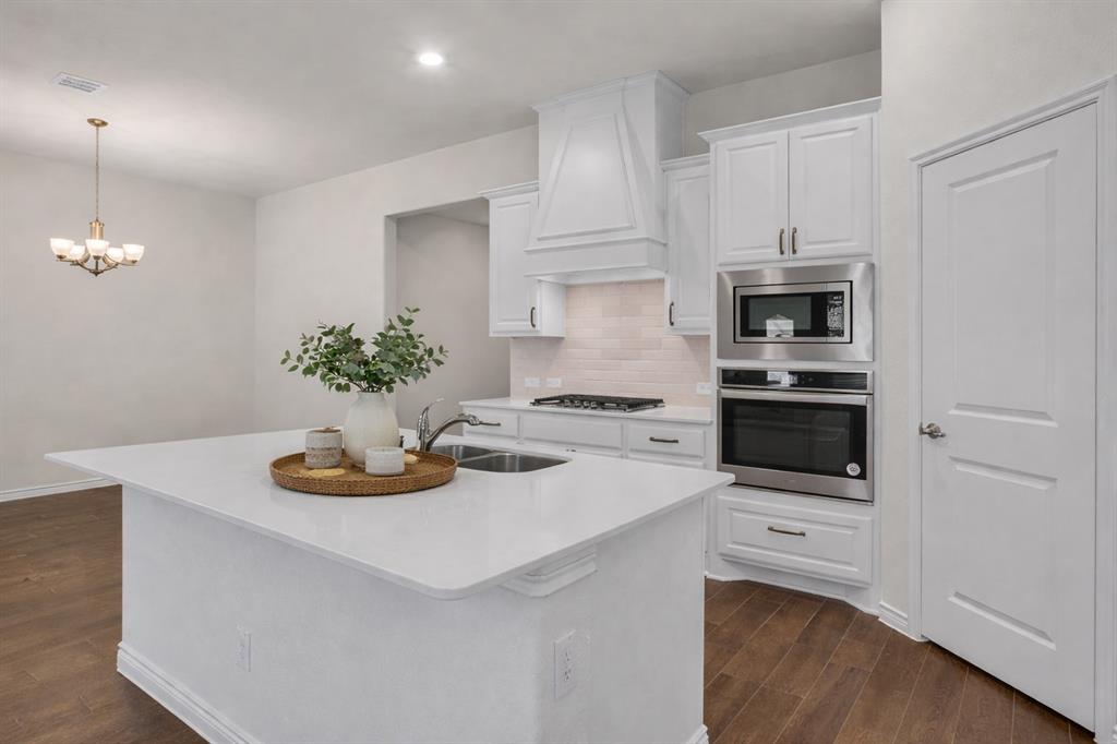 White kitchen island with an undermount sink, a gas cooktop, white shaker cabinetry, stainless steel built-in appliances, and wood-finish flooring