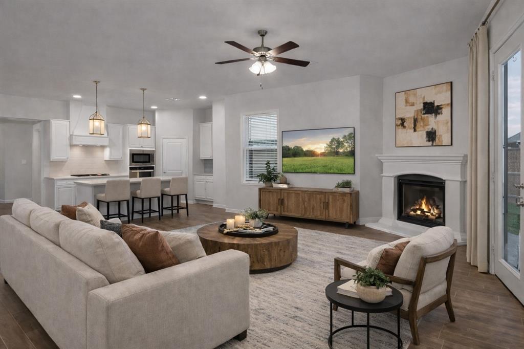 Open-concept living space featuring a white kitchen with an island, a built-in fireplace, wood-finish flooring, and a ceiling fan