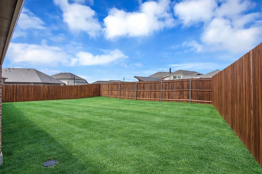 Expansive backyard featuring a manicured lawn, a stained wood privacy fence, and brick detailing on the property exterior