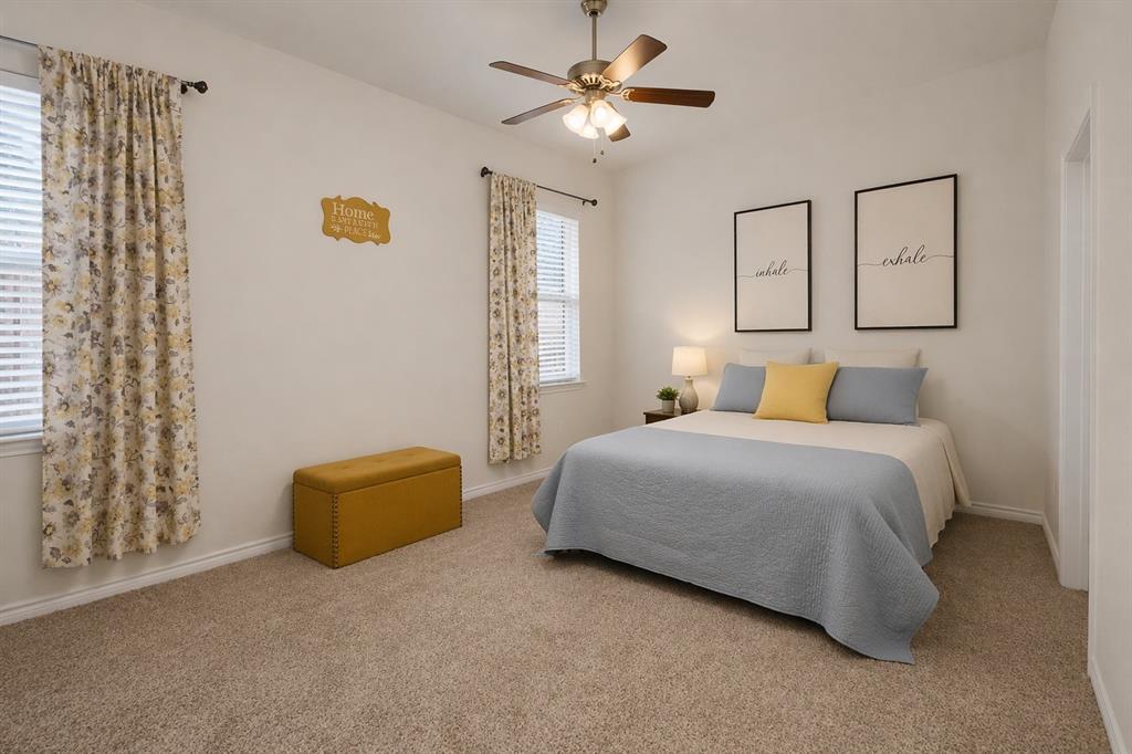 Carpeted bedroom featuring two windows with blinds, a ceiling fan with integrated lighting, and a neutral color palette
