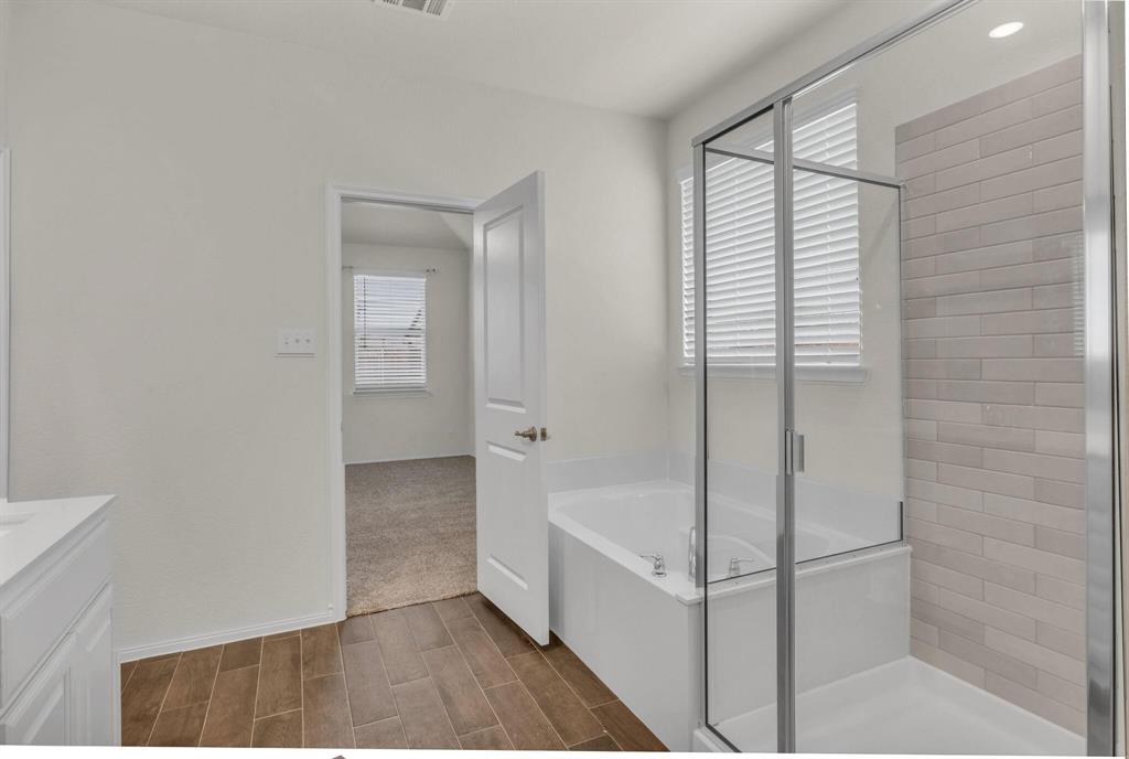 Bathroom featuring a built-in tub, separate glass-enclosed shower with subway tile surround, wood-finish tile flooring, and light-toned vanity with countertop
