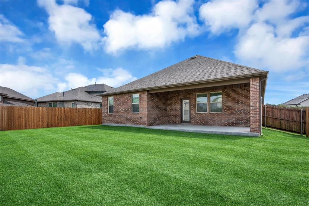 Expansive green lawn with a covered concrete patio, full brick exterior, multiple windows, and a wood privacy fence