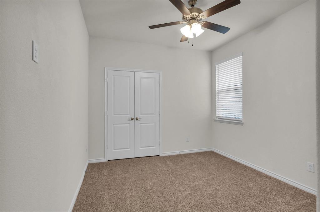 Neutral toned bedroom featuring brown carpeting, a window with horizontal blinds, white double doors, and a ceiling fan with integrated lighting