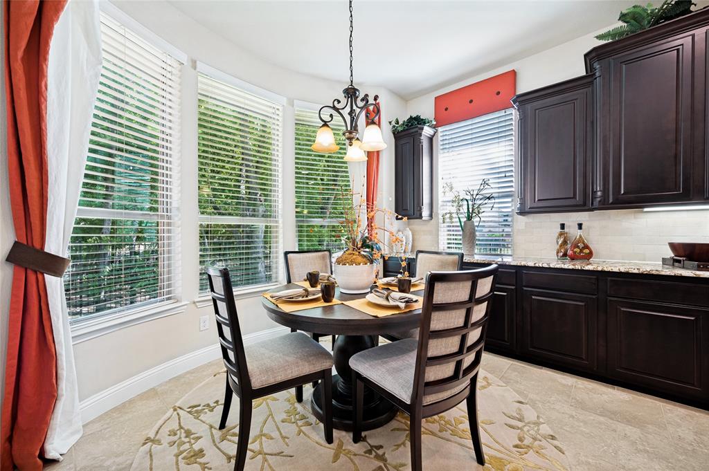 This bright and airy breakfast room features a bay window with scenic views, custom cabinetry, light-toned flooring, expansive countertops, and a serving bar area.