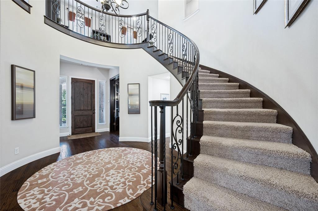 The two-story entry boasts an elegant curved staircase featuring a decorative wrought-iron railing, complemented by hand-scraped hardwood flooring, custom lighting, and a solid wood front entry door.