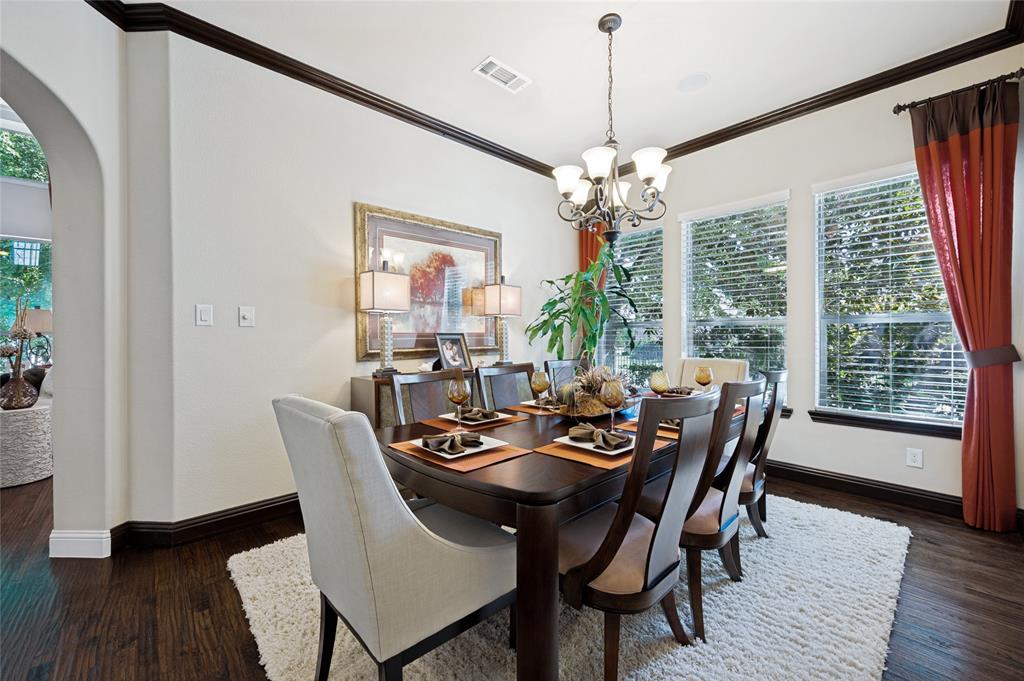 This spacious formal dining area features hand-scraped hardwood flooring, an arched entryway, a designer chandelier, and an abundance of natural light provided by multiple windows.