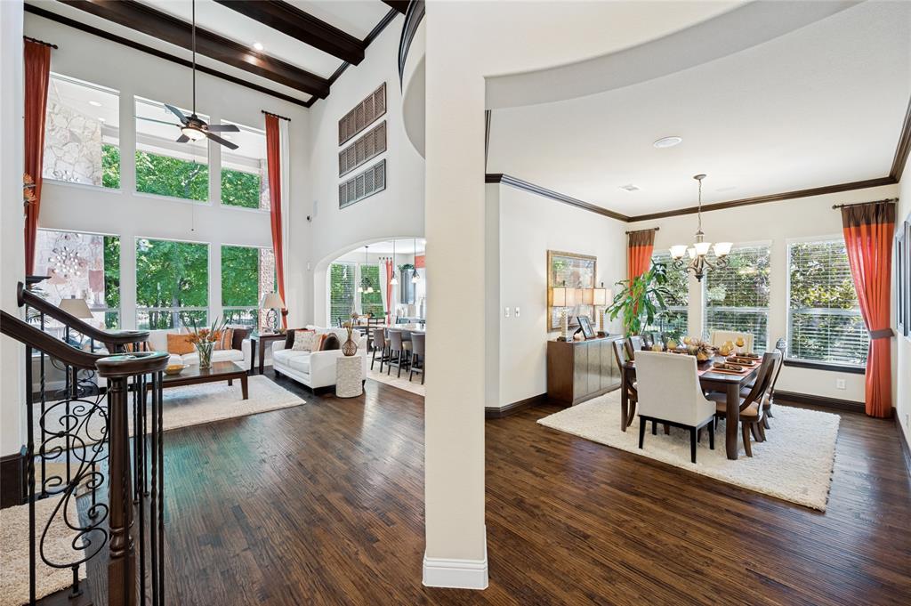 Upon entering the home, you are welcomed into a two-story living area featuring expansive windows, hardwood flooring, wood-beamed ceilings, and an elegant decorative staircase.