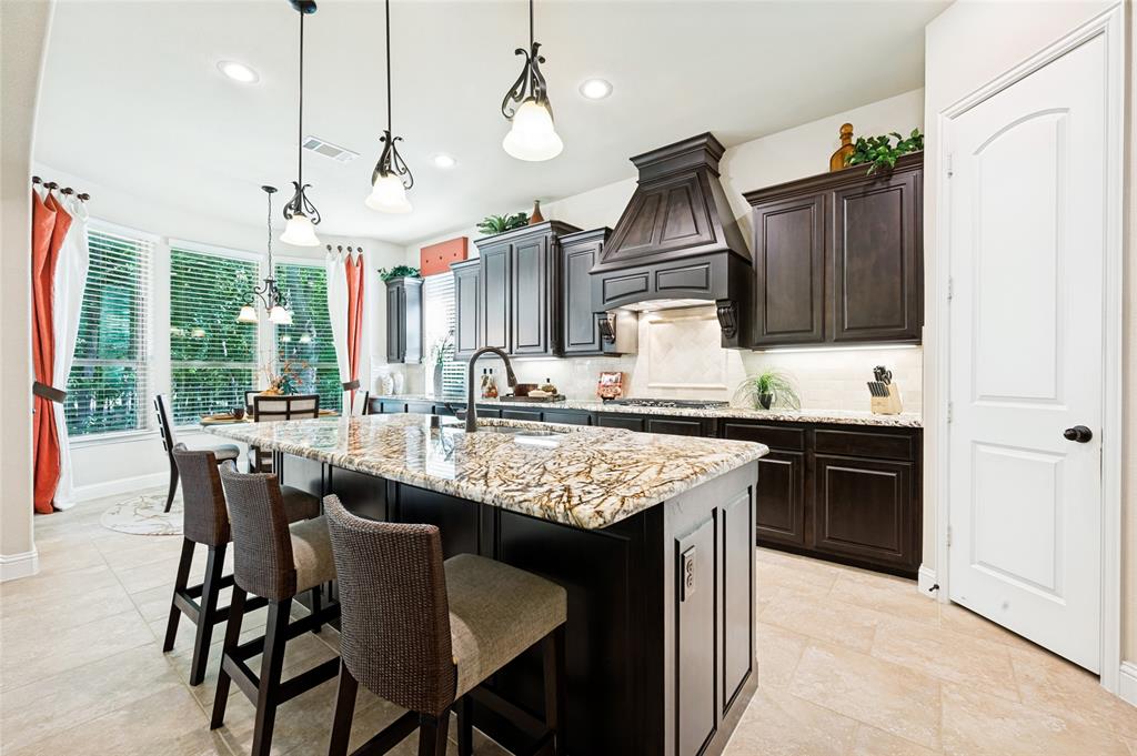The gourmet kitchen features an open concept layout seamlessly flowing into the family room, complete with a central island, granite countertops, an integrated sink, custom wood cabinetry, a decorative range hood, recessed and pendant lighting, and a spacious walk-in pantry.