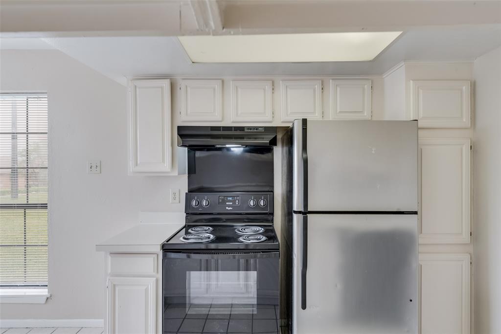 Kitchen featuring white cabinets, black range with electric cooktop, stainless steel fridge, and plenty of natural light