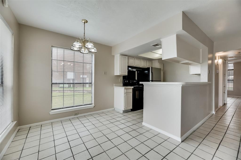 Kitchen with pendant lighting, white cabinets, light tile flooring, black range with electric cooktop, and a notable chandelier