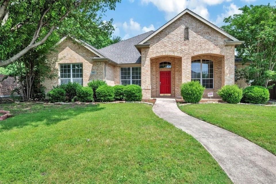 Charming brick residence featuring a welcoming red entry door, arched architectural detailing, and multi-pane windows with contrasting trim