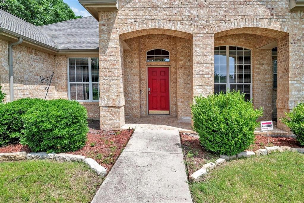 Brick exterior featuring an arched entry, a red front door, and a concrete pathway