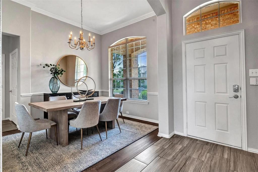 Arched window with blinds, decorative wall trim, wood-finish flooring, white paneled door, and an overhead chandelier
