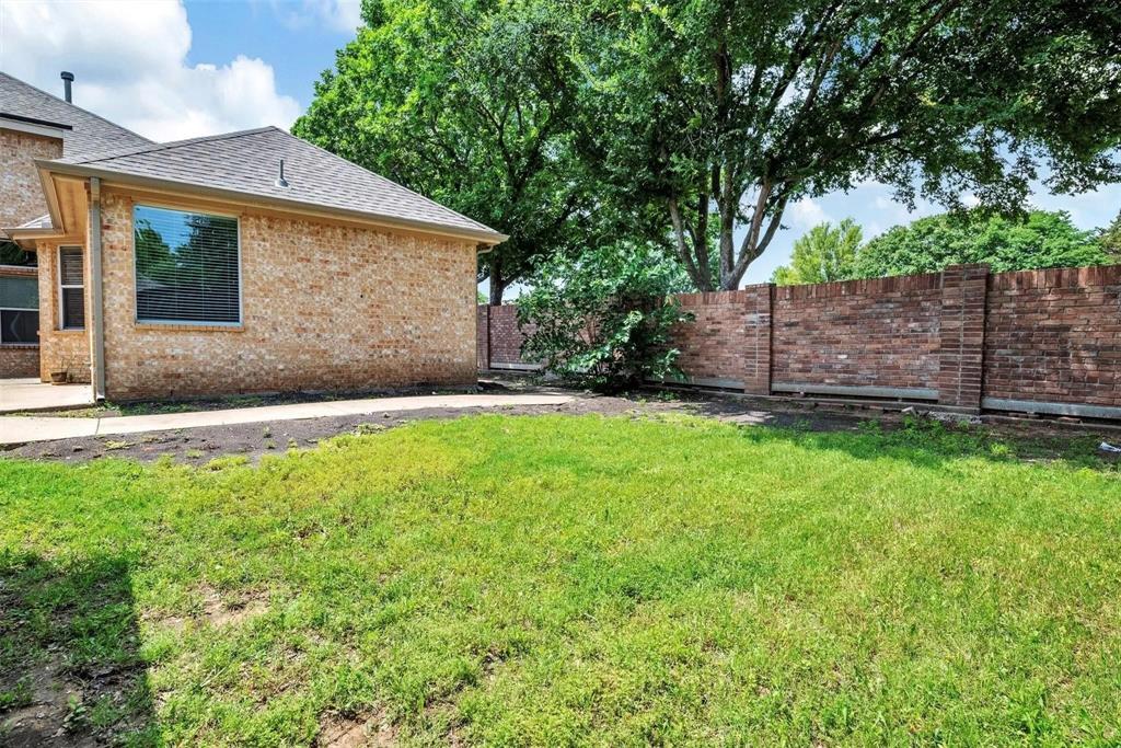 Brick exterior with a gabled roof, a large window, a concrete patio, and a brick privacy wall