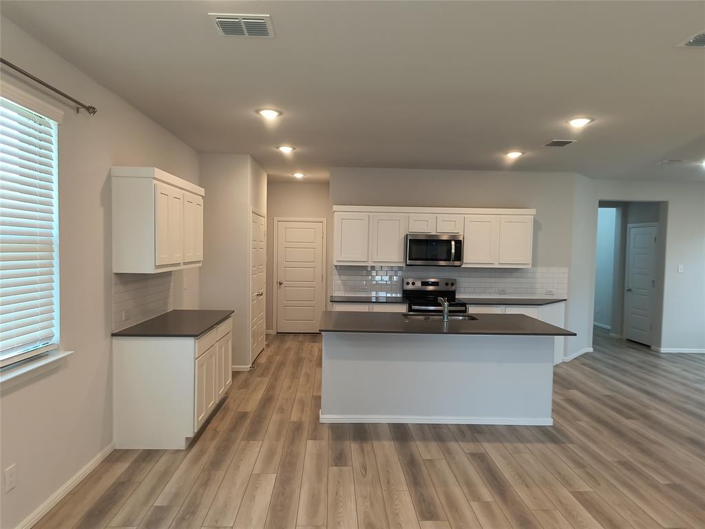 Kitchen featuring white shaker cabinetry, dark countertops, a stainless steel microwave and range, a tile backsplash, and recessed lighting Kitchen featuring white shaker cabinetry, dark countertops, a stainless steel microwave and range, a tile backsplash, and recessed lighting