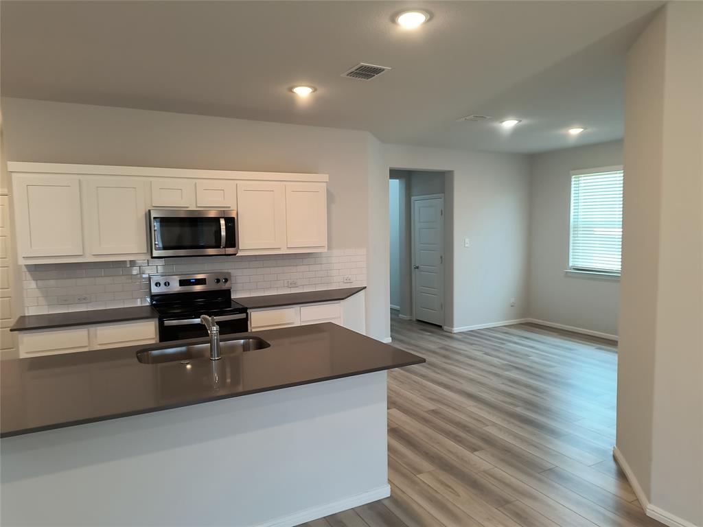 Kitchen featuring white shaker cabinetry, stainless steel appliances, subway tile backsplash, and a large island with an undermount sink Kitchen featuring white shaker cabinetry, stainless steel appliances, subway tile backsplash, and a large island with an undermount sink