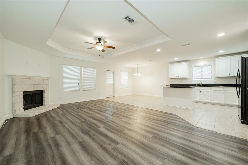 Unfurnished living room featuring a ceiling fan, a raised ceiling, crown molding, a chandelier, and light wood finished floors