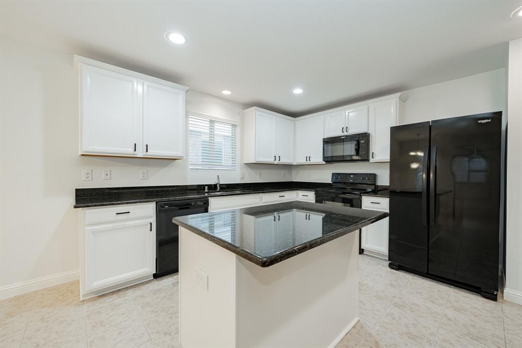 Kitchen featuring black appliances, white cabinets, dark stone countertops, recessed lighting, and a center island